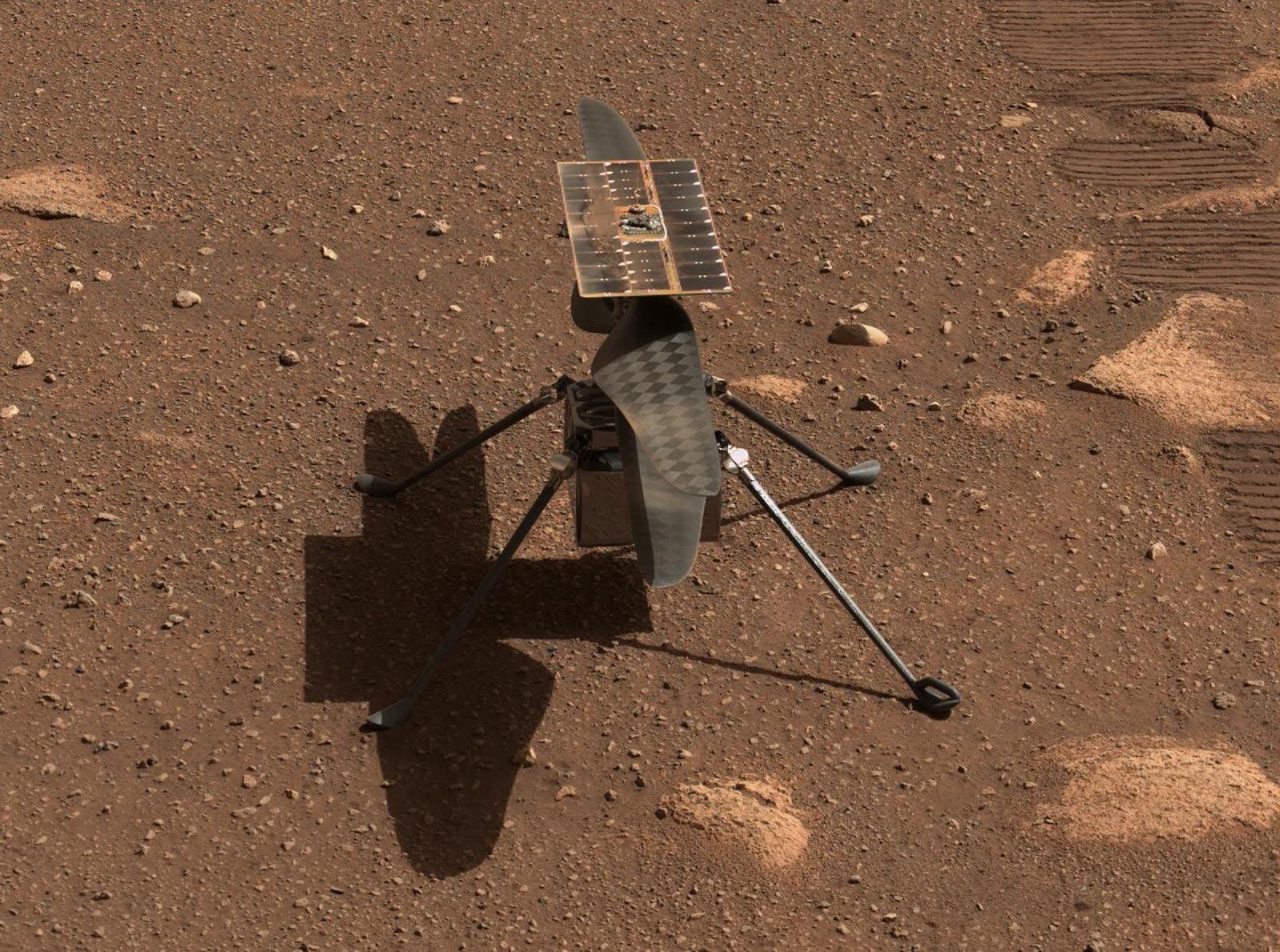 A small helicopter with two rotor blades and a solar panel standing on four thin legs on red Martian ground